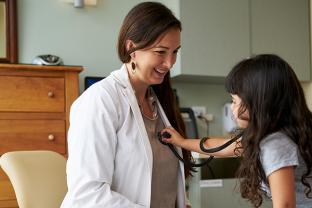 young child holding a stethoscope, placed over her pediatrician's heart